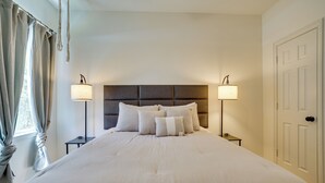 A neatly made bed with a headboard, two bedside tables with lamps, and a door to the right. - Historic Southside Fort Worth Home w/ Fenced Yard! (Fort Worth)