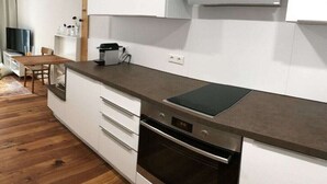 Een moderne keuken met een ingebouwde oven, een koffiezetapparaat, en een eethoek met een houten tafel en stoelen.