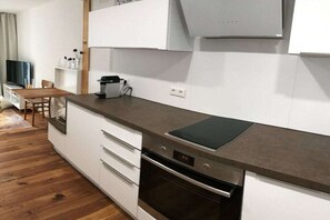 A modern kitchen with a built-in oven, a coffee maker, and a dining area with a wooden table and chairs.
