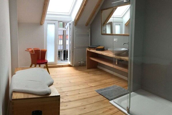 A compact room with a skylight, a wooden floor, a red chair, a white bench, and a glass shower enclosure.