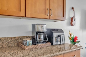 A kitchen with wooden cabinets, a coffee maker, a toaster, and a guitar on the wall. - Diredt Oceanfront 1BR with amazing views, pool, hot tub, lani and AC-Maalaea Banyans 310 (Wailuku)