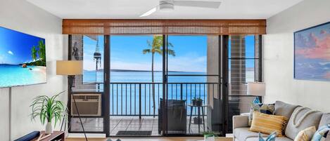 A modern living room with a view of the ocean, a balcony with a railing, and a ceiling fan.