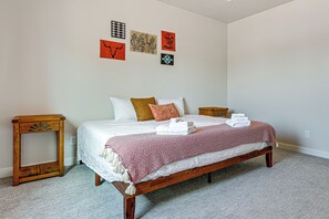A bedroom with a wooden bed, white bedding, a red and white patterned throw, and a small wooden nightstand. - Explore Glen Canyon/Lake Powell! Red River Retreat (Page)