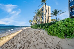 A beachfront hotel with a sandy beach, palm trees, and a clear blue sky. - Oceanfront 1BD with Panoramic Ocean & Sunset Views -Mahana 406 (Lahaina)