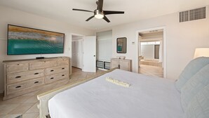 Un dormitorio con cama, cómoda, televisor y ventilador de techo.