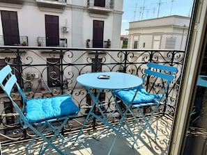 A balcony with a round table and two chairs, a potted plant, and a window with blinds. - L'altra porta (Naples)