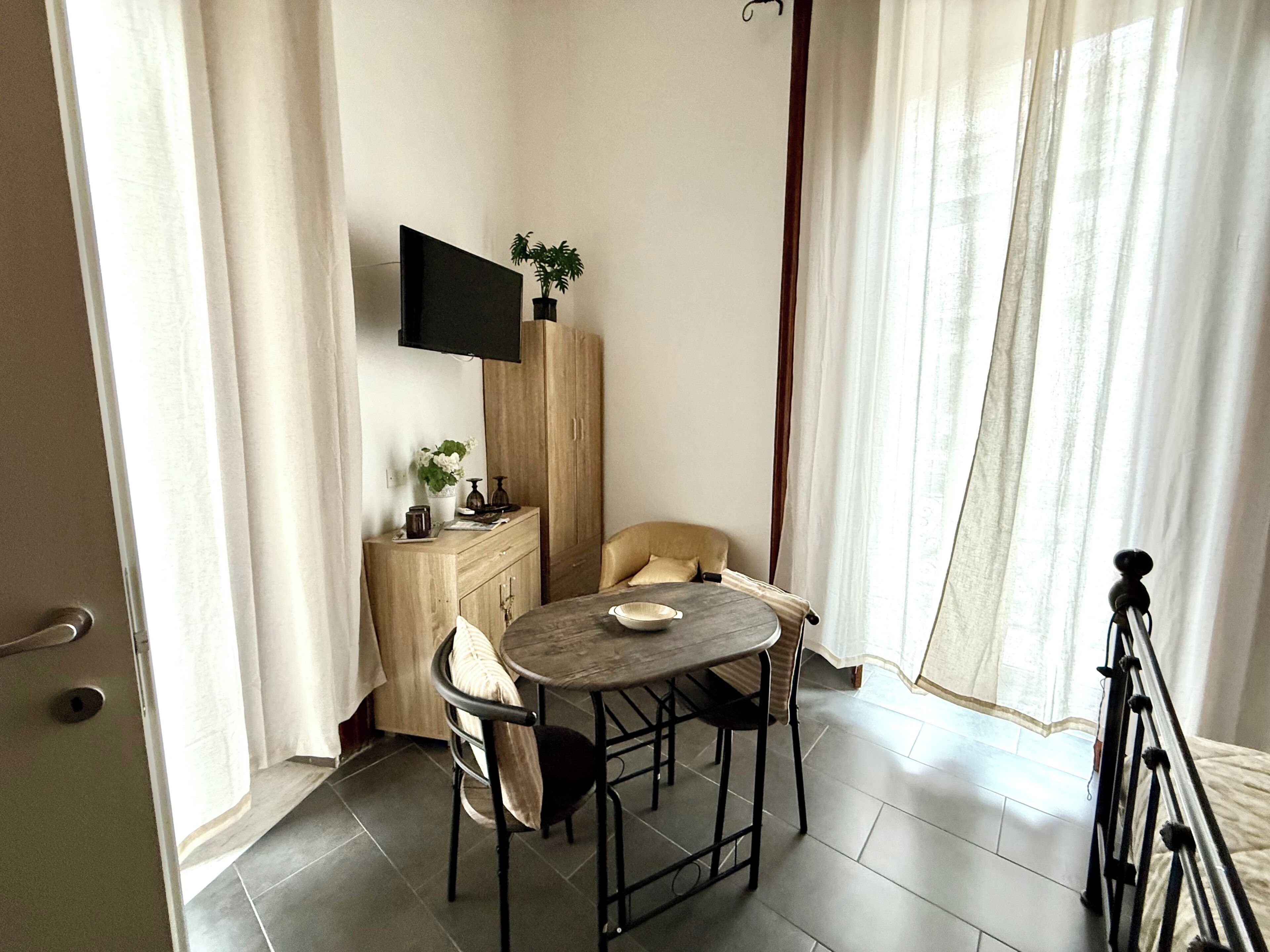 A small dining area with a table, chairs, a television mounted on the wall, and a cabinet with a plant.