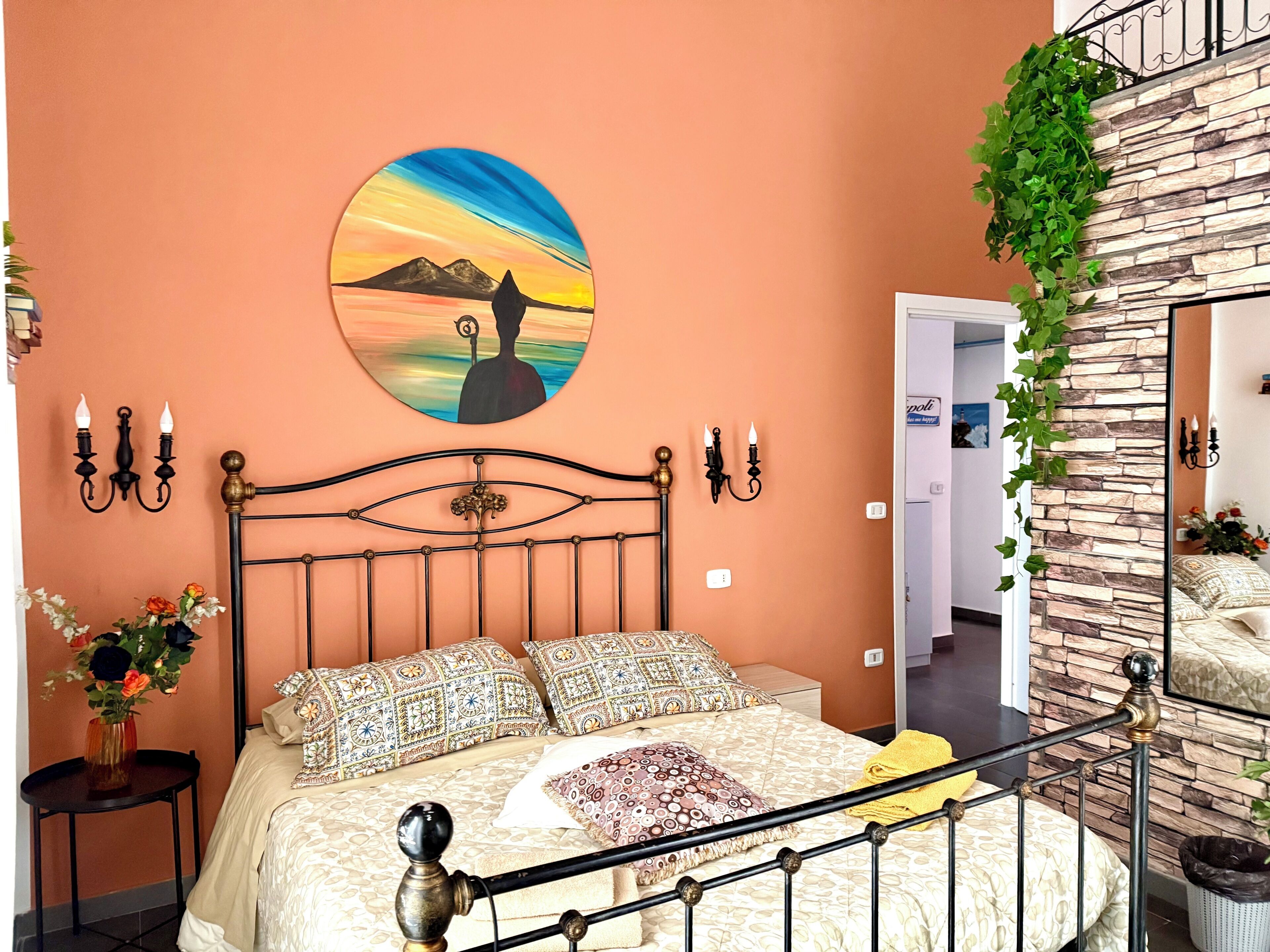 A bedroom with a bed, a wall-mounted painting, and a staircase with a stone wall.