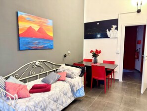 A room with a bed, a dining table with chairs, a vase with flowers, and a painting on the wall. - L'altra porta (Naples)