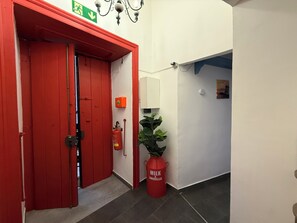 A red door with a green emergency exit sign, a fire extinguisher, and a potted plant. - L'altra porta (Naples)