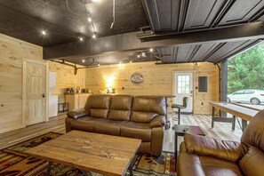 A cozy cabin interior with a leather sofa, a wooden dining table, and a kitchen area.