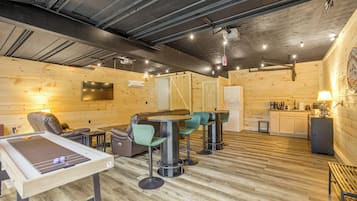 Une pièce chaleureuse avec un plancher en bois, un téléviseur à écran plat fixé au mur, un canapé, une table avec des chaises et un coin cuisine équipé d’un réfrigérateur et d’une machine à café.