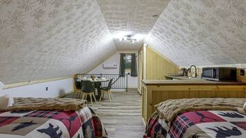 Une chambre confortable située dans les combles, avec deux lits, une table à manger et un coin cuisine.