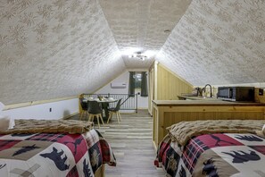 A cozy attic bedroom with two beds, a dining table, and a kitchenette.