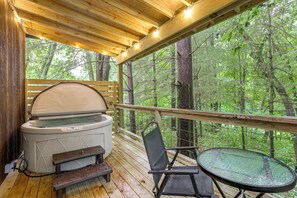 A wooden deck with a hot tub, a table, and a chair, overlooking a forest.