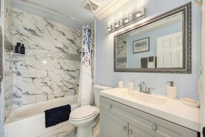 Een badkamer met een douchewand van marmer, een wit toilet, een wastafel met spiegel en een bad.