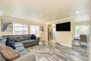 A spacious living room with a gray sectional sofa, a glass coffee table, and a peacock painting on the wall. - Near Golden 1 Center! Modern Home w/ Ping-Pong (Sacramento)