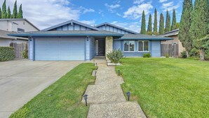 A single-story house with a blue garage, a front porch, and a well-maintained lawn. - Near Golden 1 Center! Modern Home w/ Ping-Pong (Sacramento)