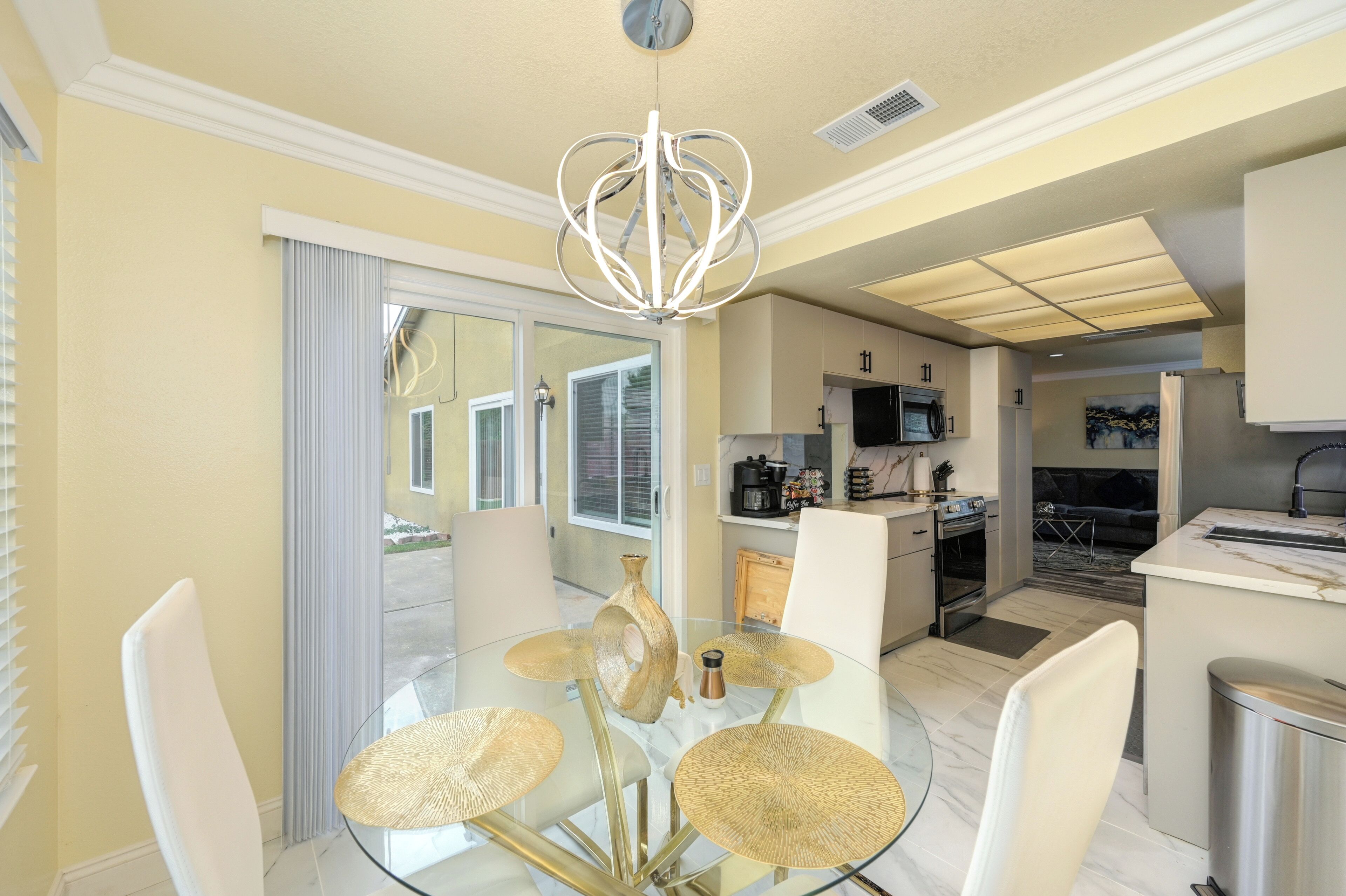 A modern kitchen with stainless steel appliances, a dining area with a glass table and chairs, and a sliding glass door leading to a patio.