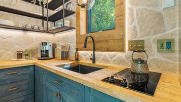 A modern kitchen with a stone wall backsplash, a built-in sink, and a window overlooking greenery.