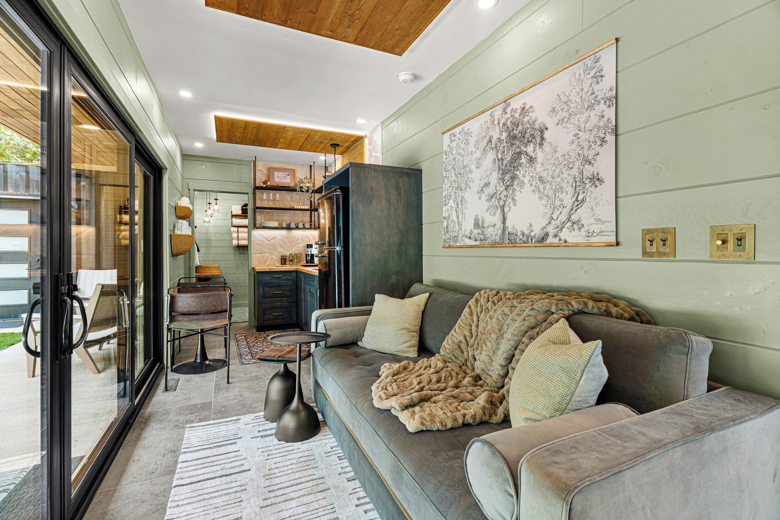 A modern living room with a grey sofa, a large abstract painting, and a dining area with a wooden table and chairs.