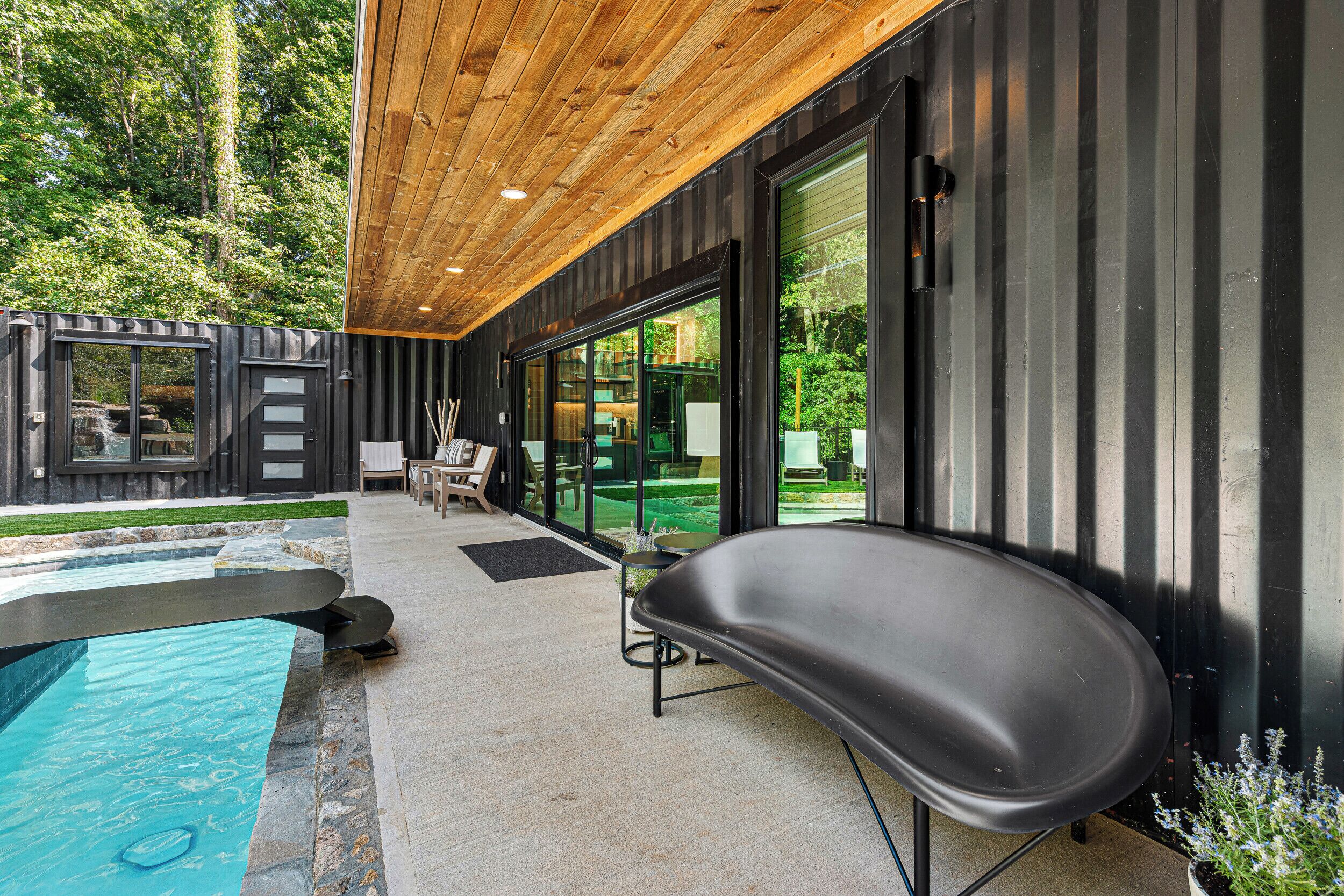 Een modern buitenzwembad met houten overkapping, een lounge stoel en een glazen patio.