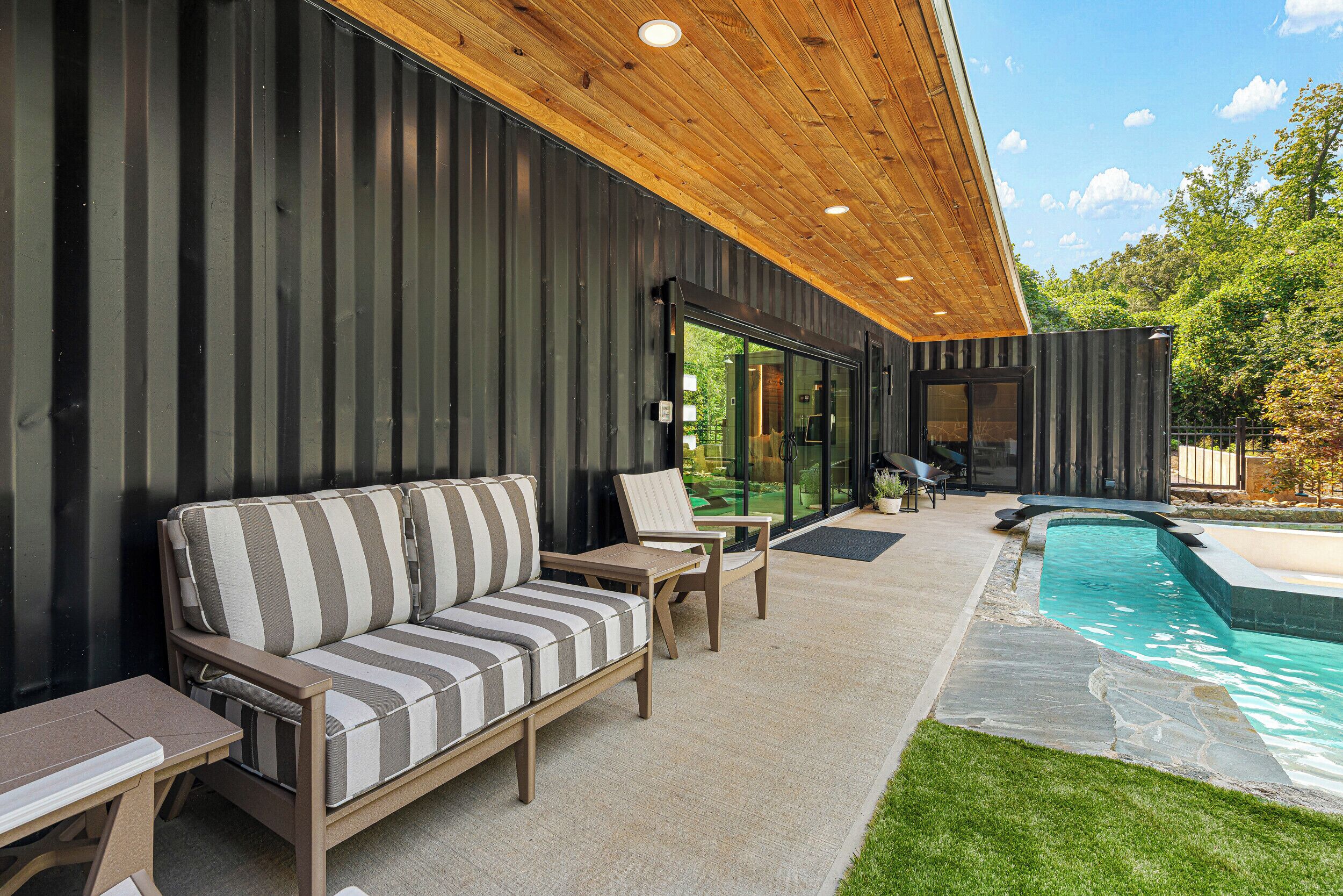 A modern outdoor seating area with a pool, wooden ceiling, and metal walls.