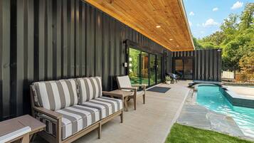 A modern outdoor seating area with a pool, wooden ceiling, and metal walls.