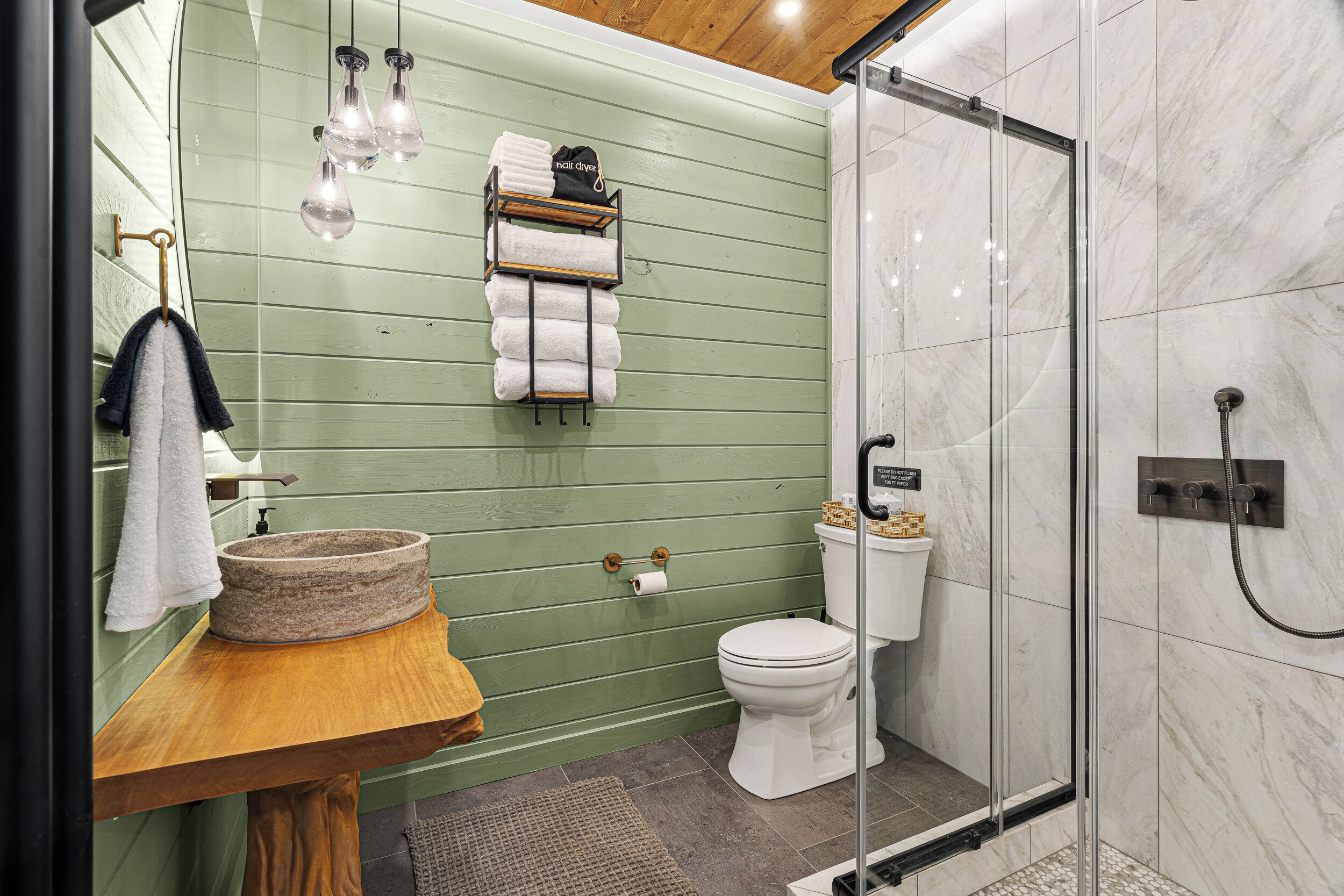 A bathroom with a wooden vanity, a glass shower enclosure, and a green wall.