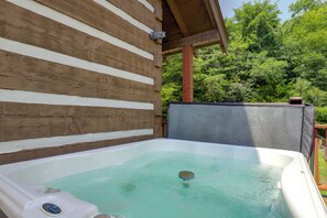 Ein Whirlpool mit Holzverkleidung, Metallabdeckung und Blick auf grüne Vegetation im Hintergrund.