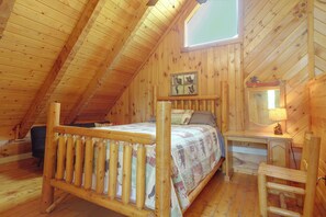 A wooden cabin with a sloped ceiling, a bed with a quilt, a nightstand with a lamp, and a window with a view. - 1 Mi to Dollywood! Hot Tub Hideaway in Smokies (Sevierville)