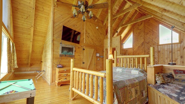 Interior de cabana de madeira com cama, televisão, mesa de bilhar e janela.