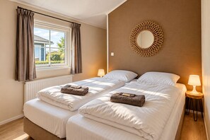Een tweepersoonskamer met twee bedden, een raam met gordijnen, een spiegel aan de muur en nachtlampjes.