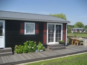 Uma casa moderna com fachada escura, molduras de janela vermelhas e um deck de madeira.