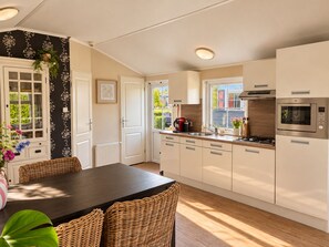 A modern kitchen with a dining area, featuring a built-in microwave, a coffee machine, and a window with a view of the outside. - Detached chalet with a hardwood terrace in the car-free heart of Giethoorn. Features a fully equipped kitchen with a dishwasher, a comfortable bedroom with a double bed, and a private washing machine in the storage room. The perfect base for a relaxi (Giethoorn)