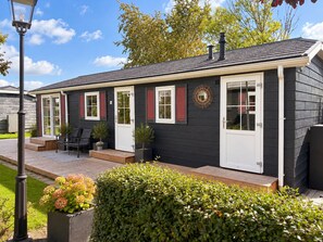 Een tweelaags huis met een donkere gevel, een veranda met een bankje en een kleine tuin.