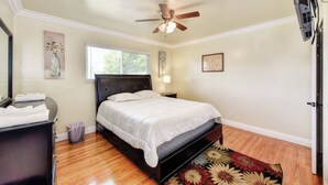 Een slaapkamer met een bed, plafondventilator, raam en een wandlamp.