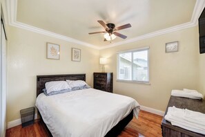 Ein Schlafzimmer mit einem Bett, einem Deckenventilator, einem Fenster mit Jalousien und einem Nachttisch.