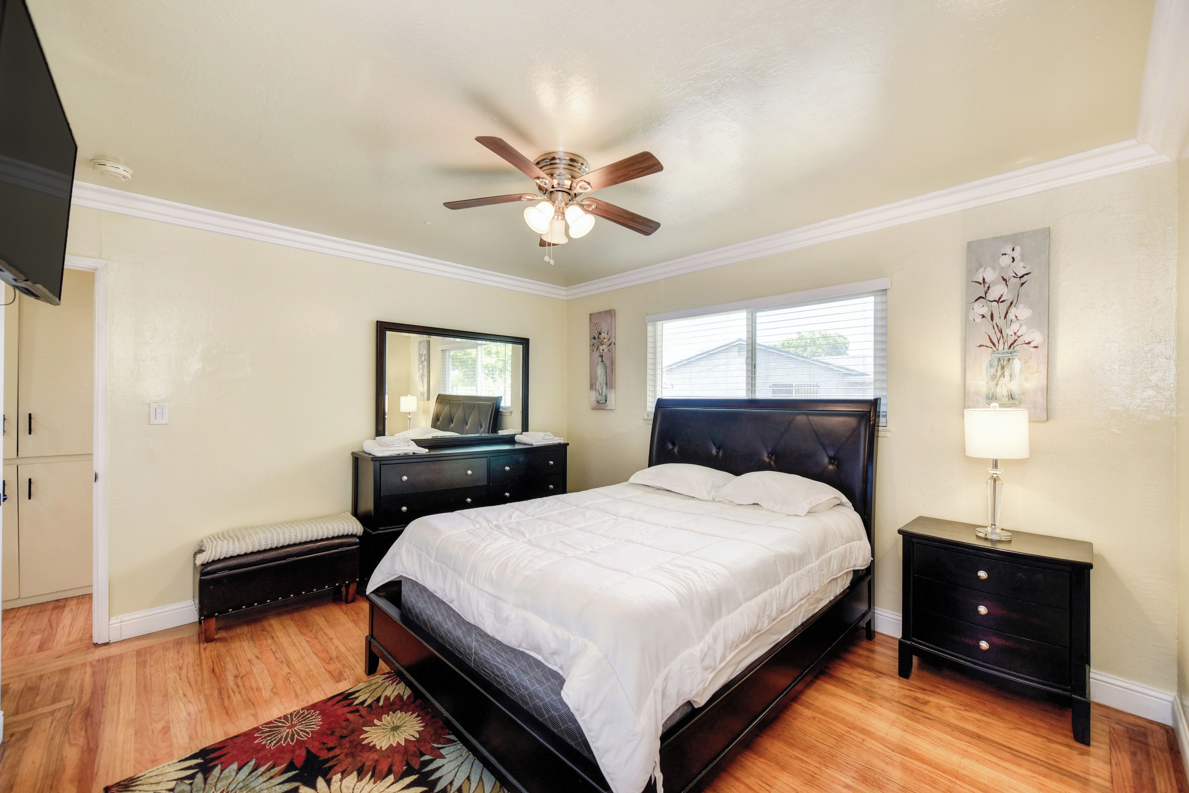 A bedroom with a bed, a dresser, a nightstand, a ceiling fan, and a window.