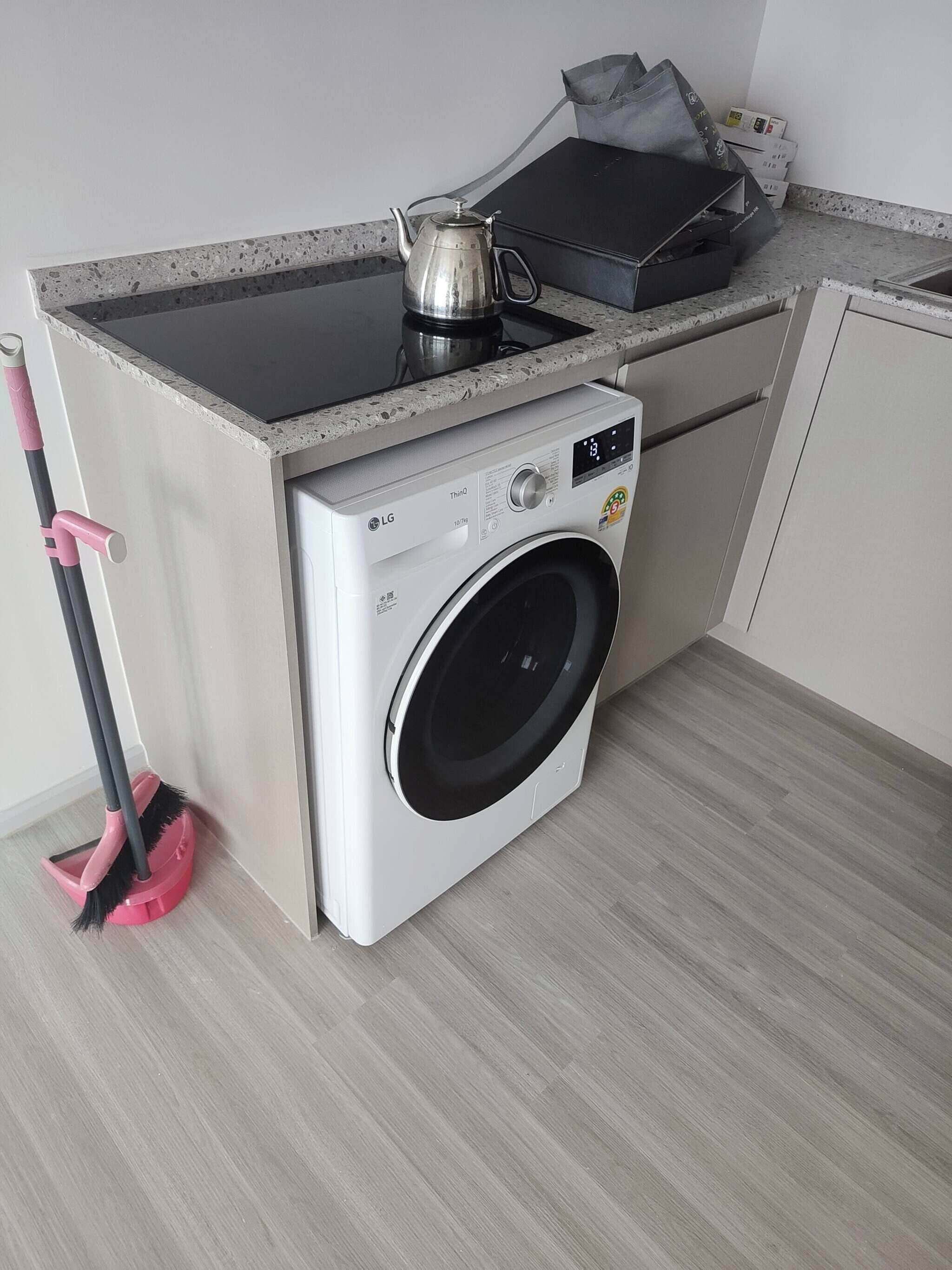 A compact kitchen with a built-in washing machine, a kettle, and a mop.