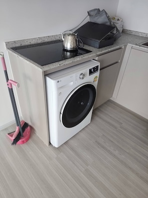 A compact kitchen with a built-in washing machine, a kettle, and a mop. - Exclusive Holiday House in Thon Buri with River Views (Thon Buri)