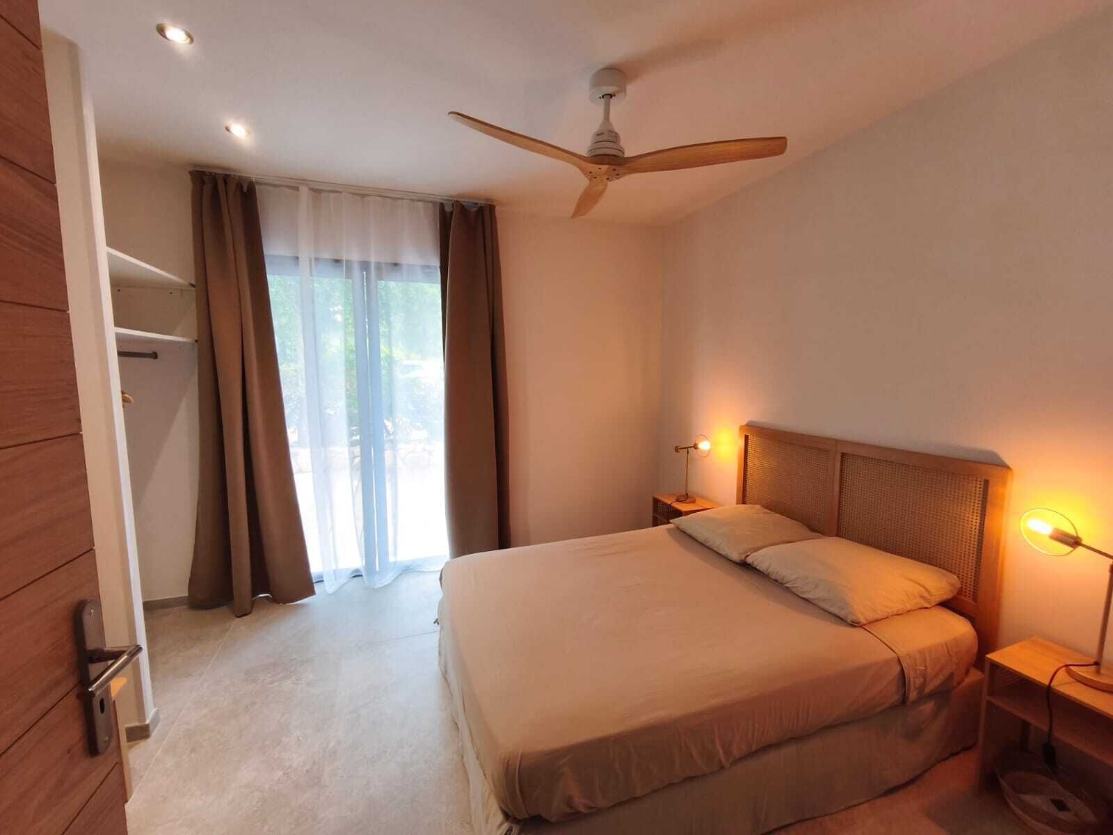 A bedroom with a bed, a ceiling fan, a nightstand with a lamp, and a wardrobe.