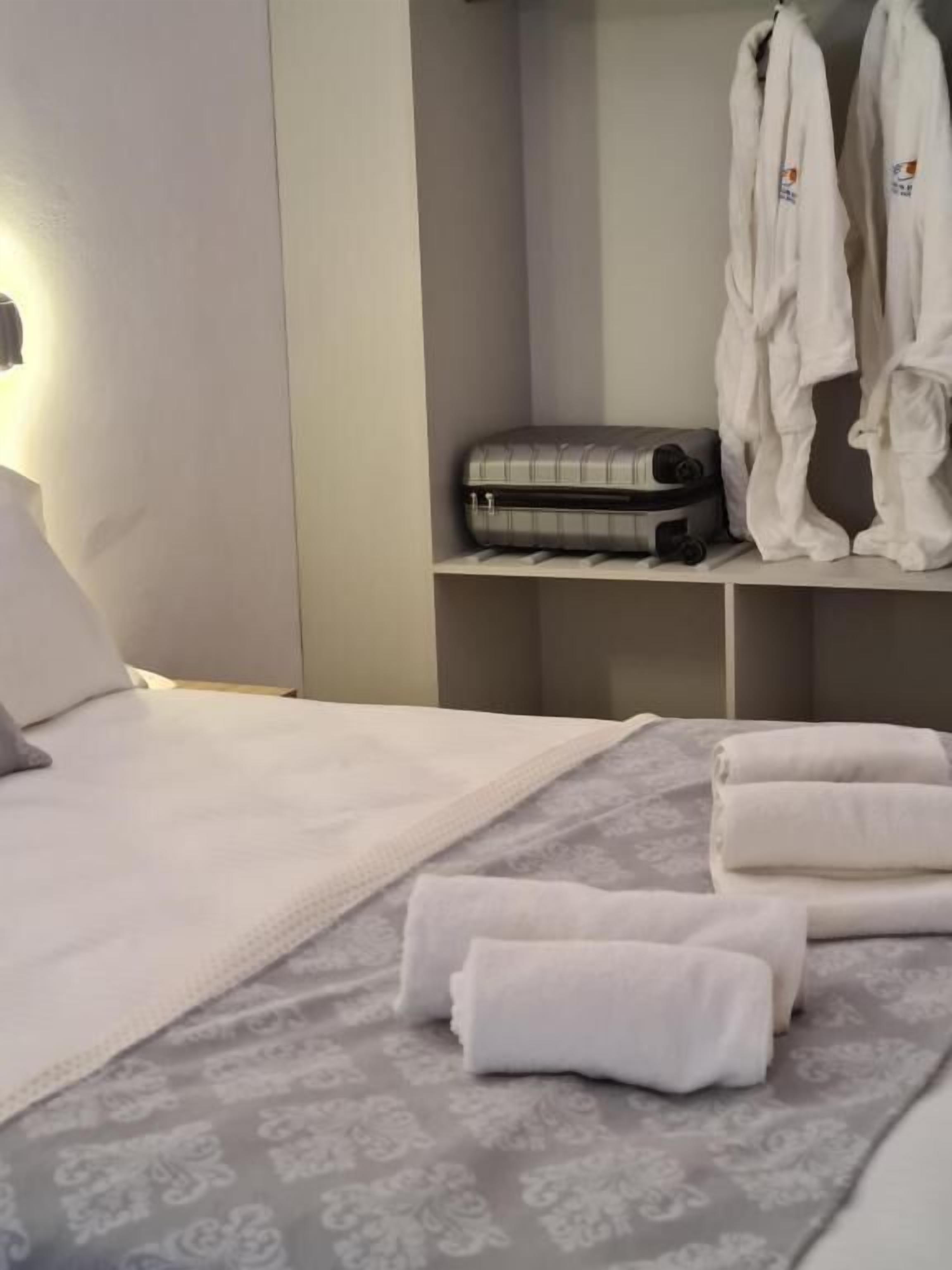 A neatly made bed with a patterned bedspread, a bedside lamp, and a suitcase on a shelf.