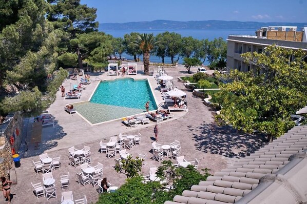 A pool area with lounge chairs and umbrellas, surrounded by trees and a view of the sea.