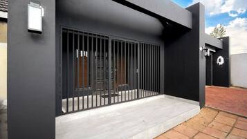 Un edificio moderno con una reja metálica, acceso de hormigón y una zona pavimentada.