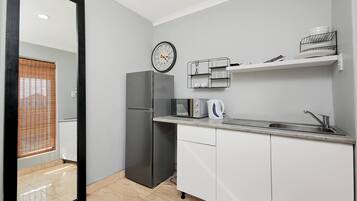 Cocina compacta con refrigerador, microondas, hervidor y un lavamanos pequeño.
