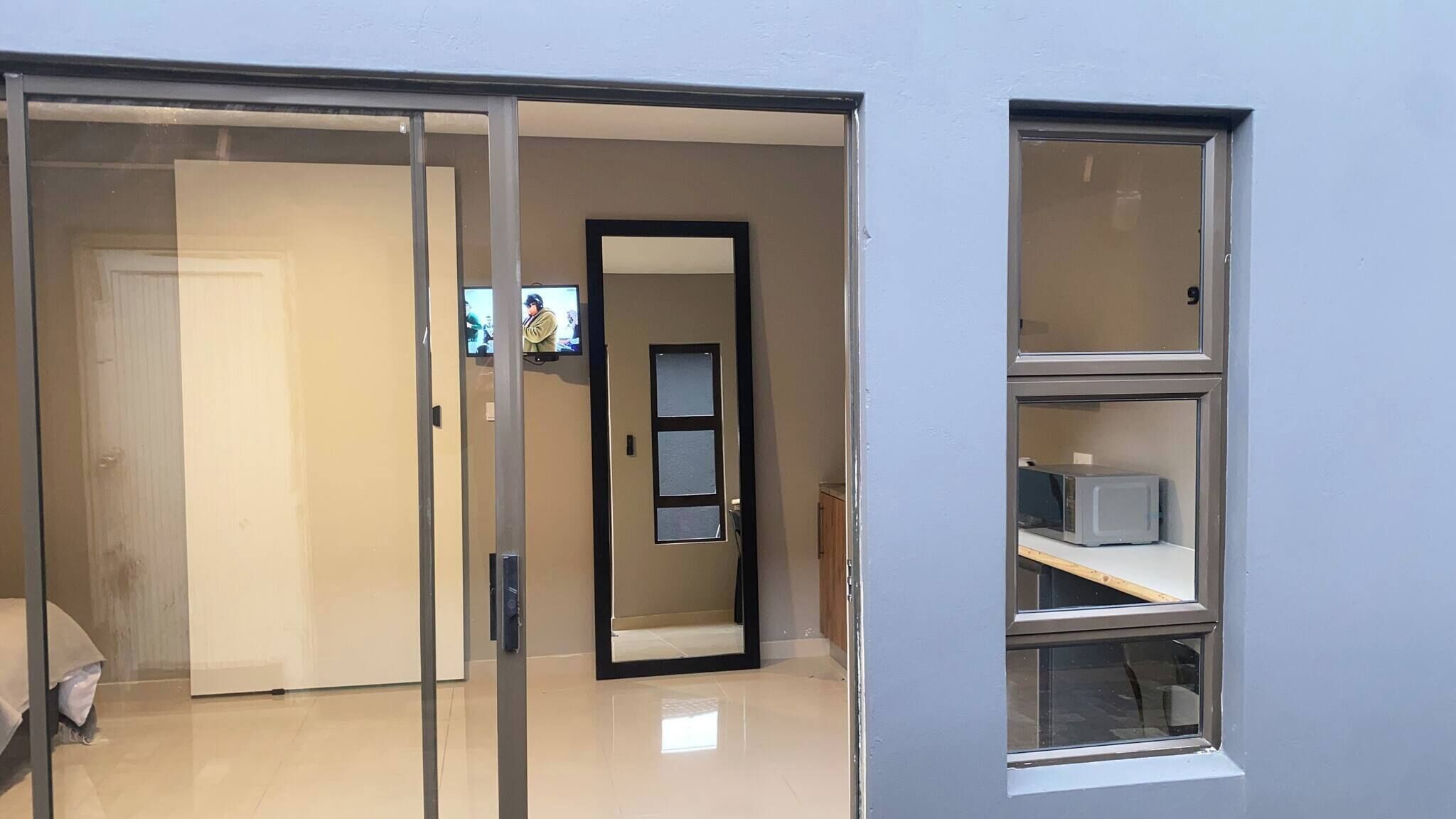 Una habitación con puerta corredera que da a un baño, una ventana pequeña con microondas y un televisor montado en la pared.