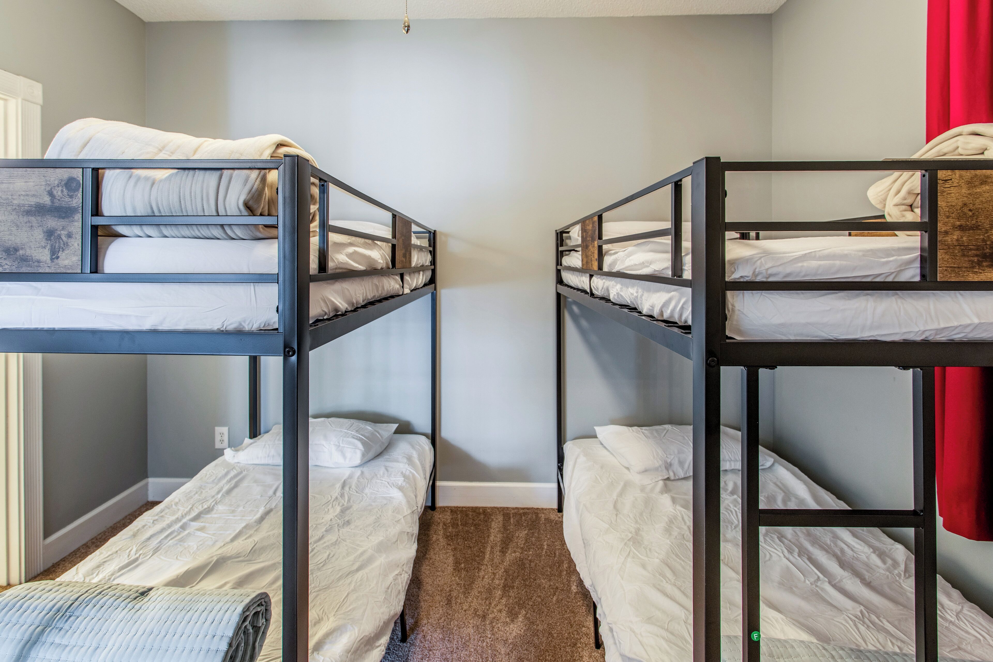 A room with two bunk beds, a carpeted floor, and a red curtain.
