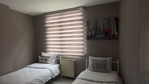 Ein Schlafzimmer mit zwei Einzelbetten, einem Heizkörper, einem Fenster mit Jalousien und einem Bild an der Wand.