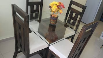 Uma mesa de jantar com tampo de vidro, rodeada por cadeiras de madeira com assentos acolchoados.
